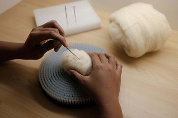 Person engaged in needle felting craft, shaping wool with a needle on a felting mat.